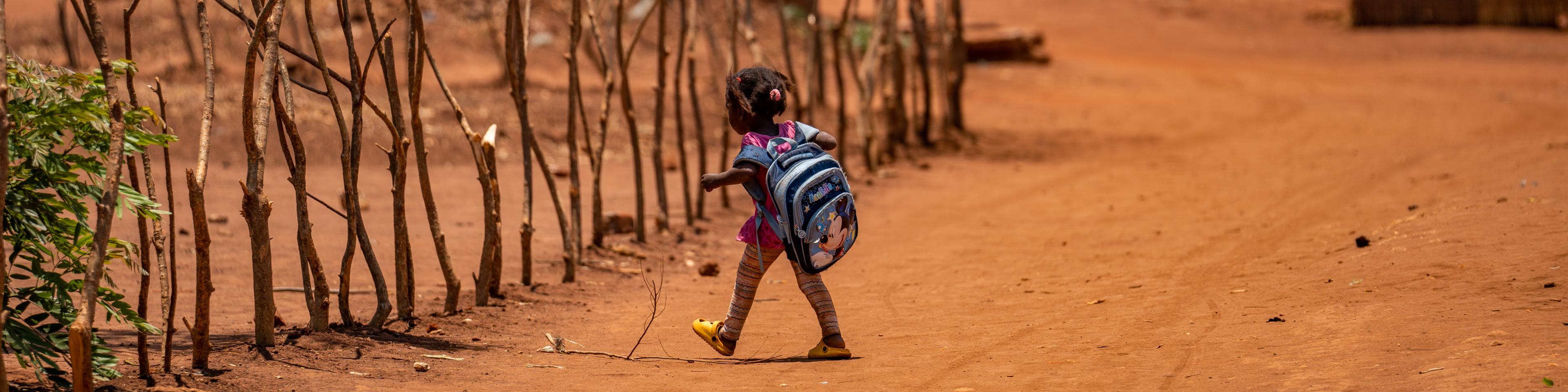 Kleiner Mädchen mit Rucksack auf staubigem Weg