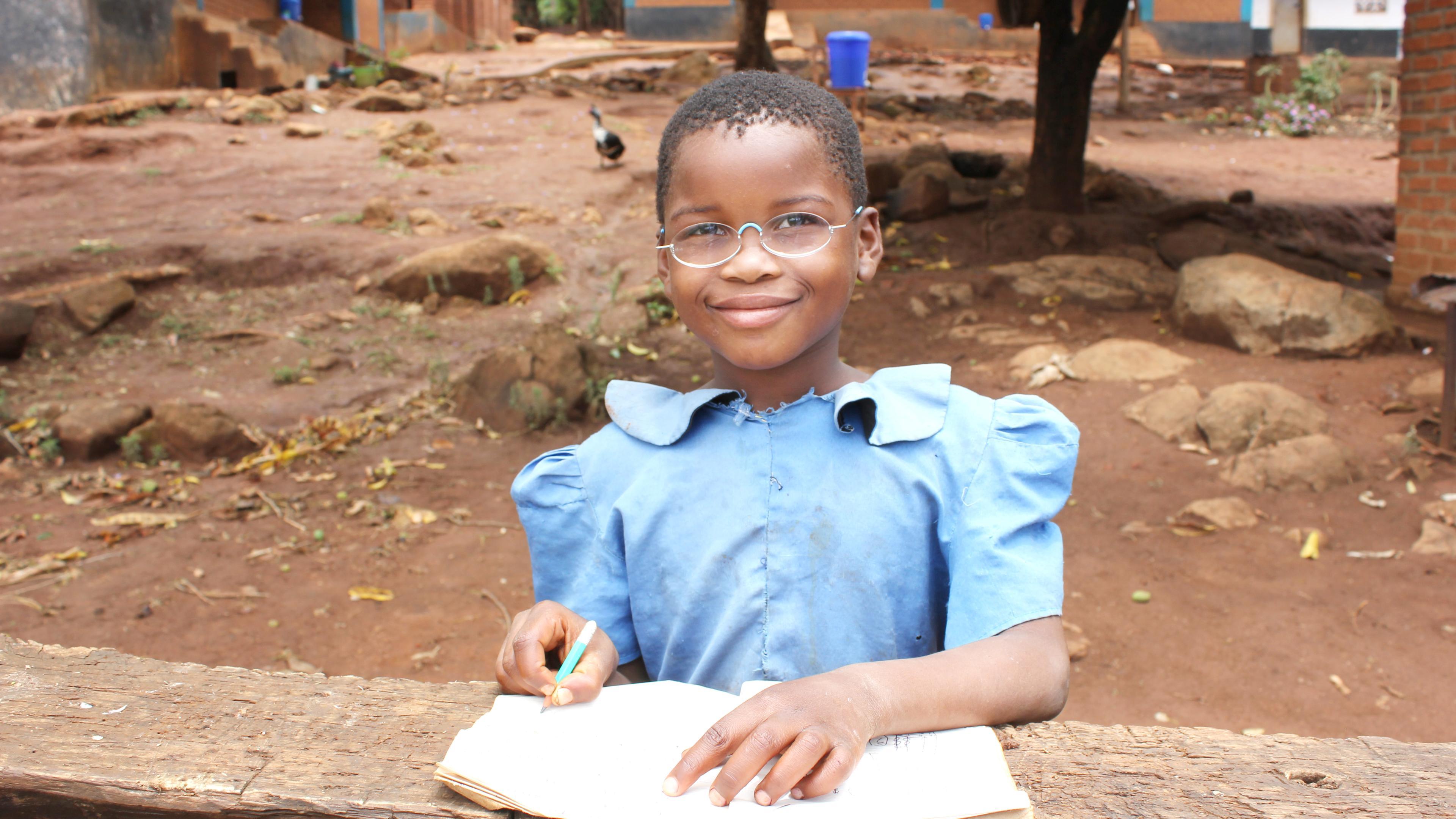 Schülerin aus Malawi, mit Schulheft und Stift, trägt EinDollarBrille
