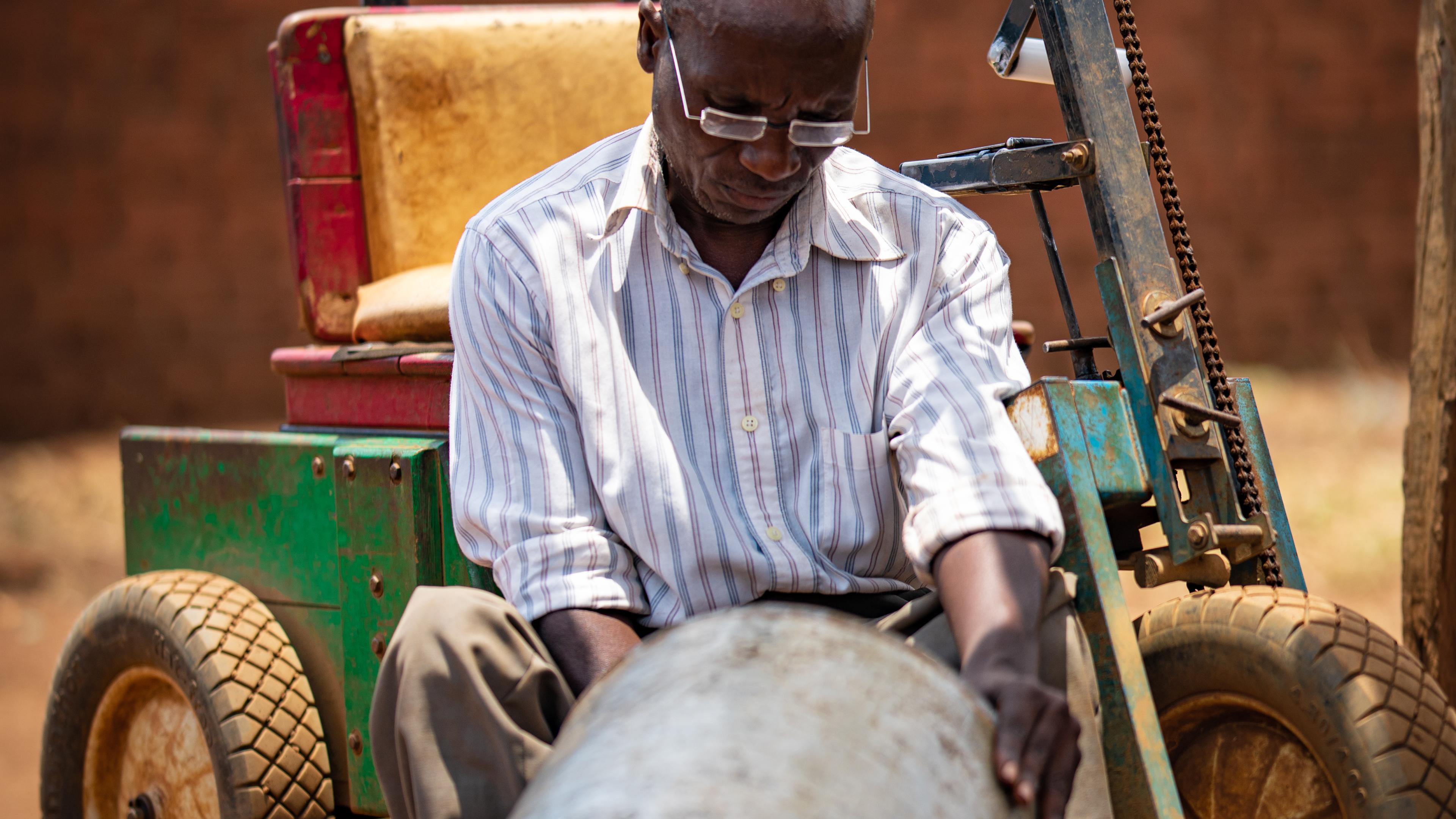 Malawian man with glasses works sheet metal with a hammer