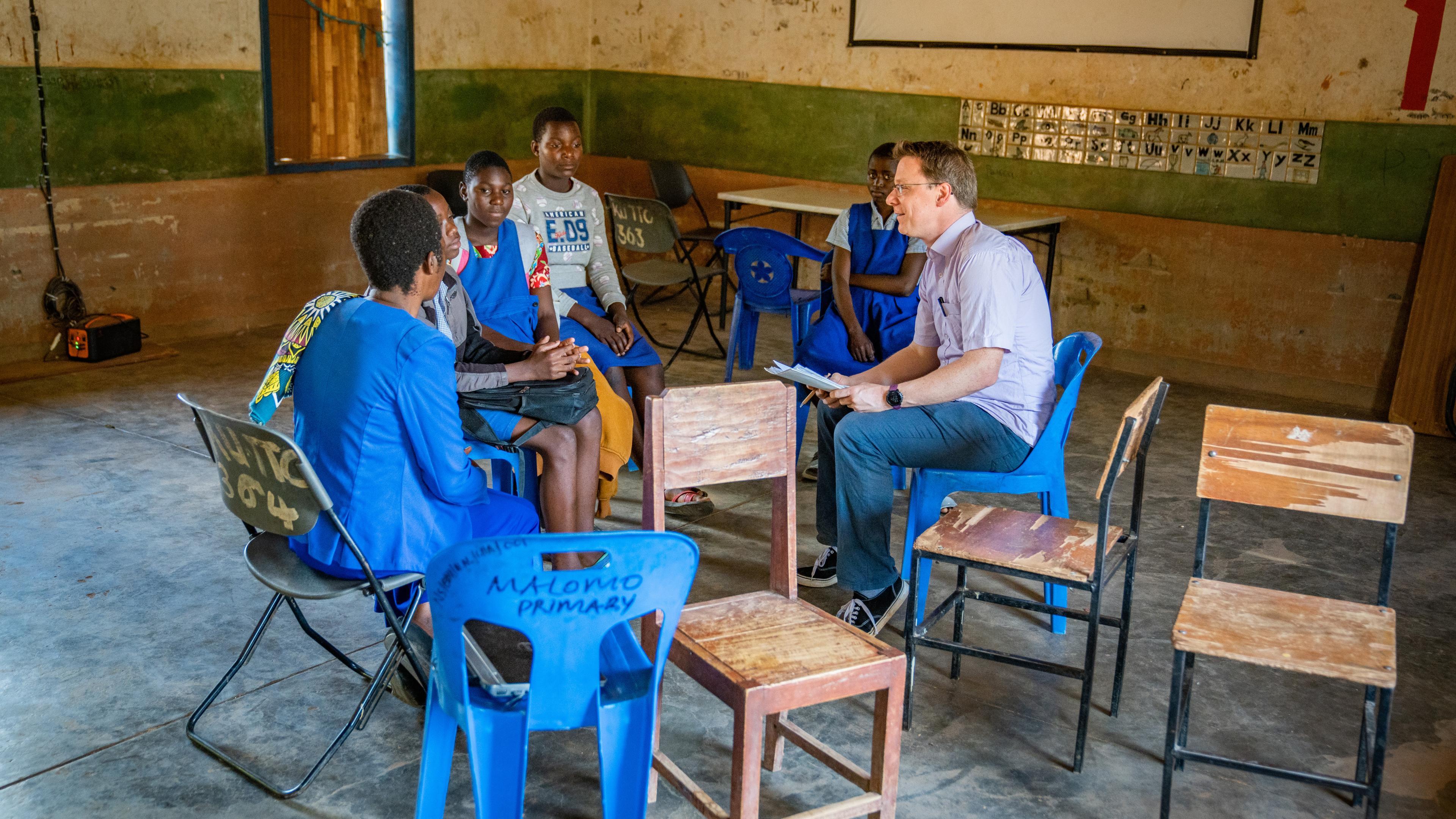 Schulkinder in Malawi sitzen um Mann, der etwas erklärt