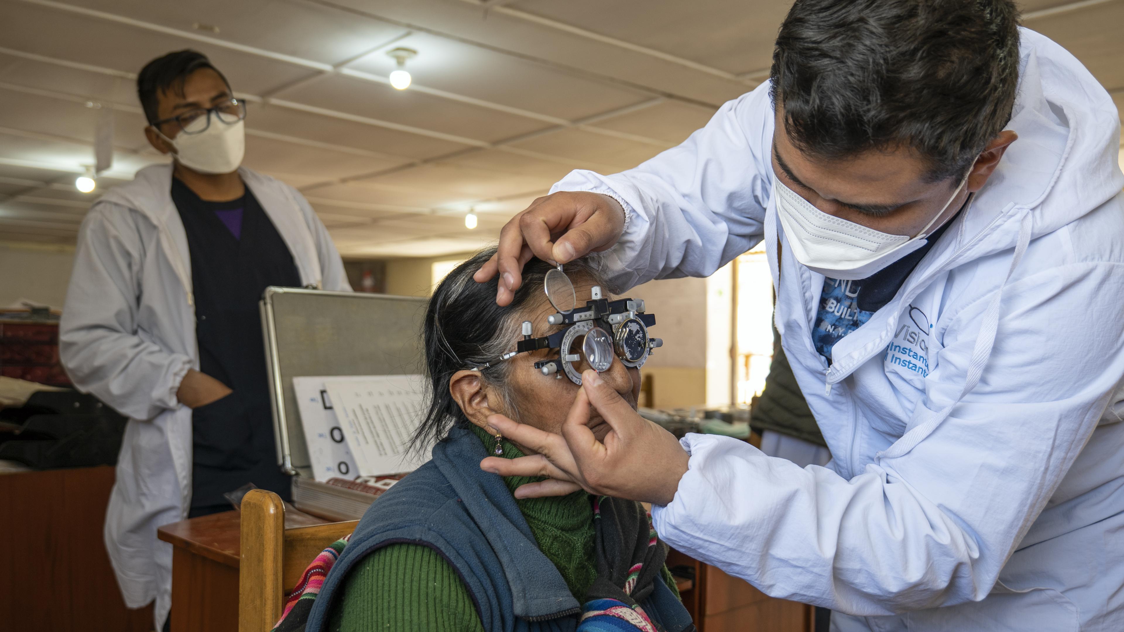 Mitarbeiter von GoodVision Peru setzt Linse in Probelinsenrahmen, Patientin blickt hindurch