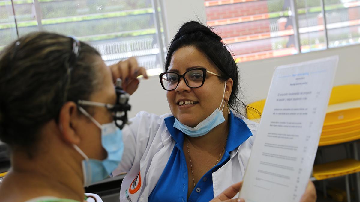 Mitarbeiterin von Lentes al Instante Bolivien mit einer Patientin, die eine optische Messbrille trägt und etwas liest