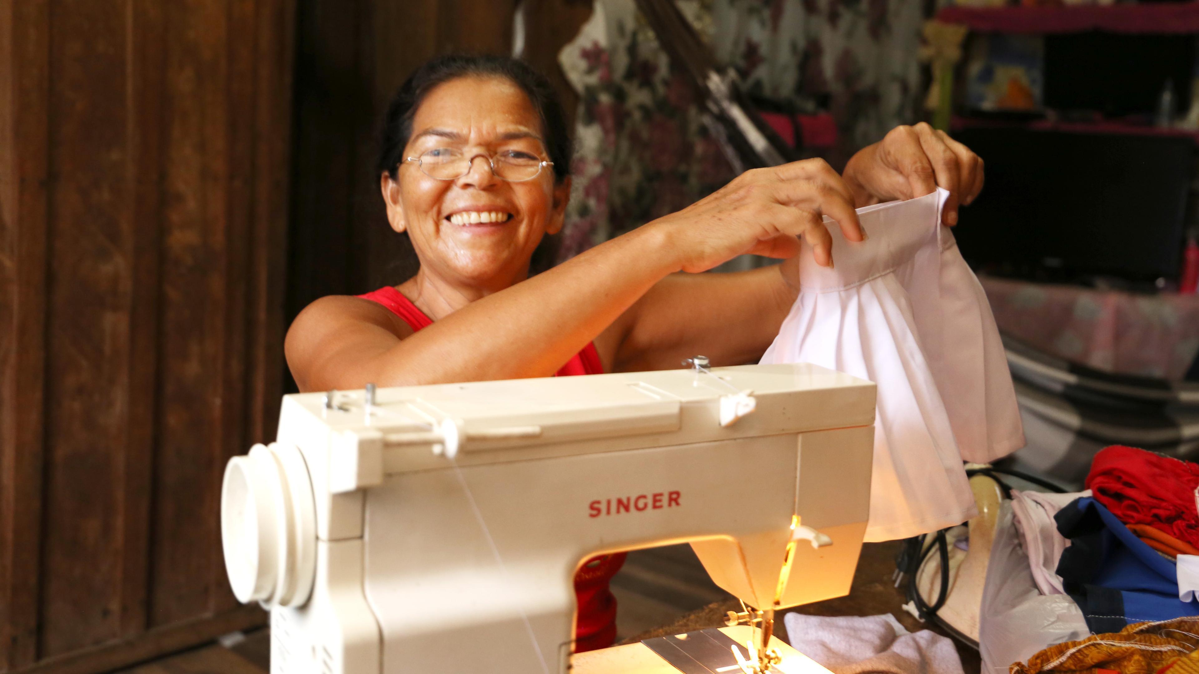 Frau sitzt vor Nähmaschine, freut sich, hält ihre Arbeit hoch