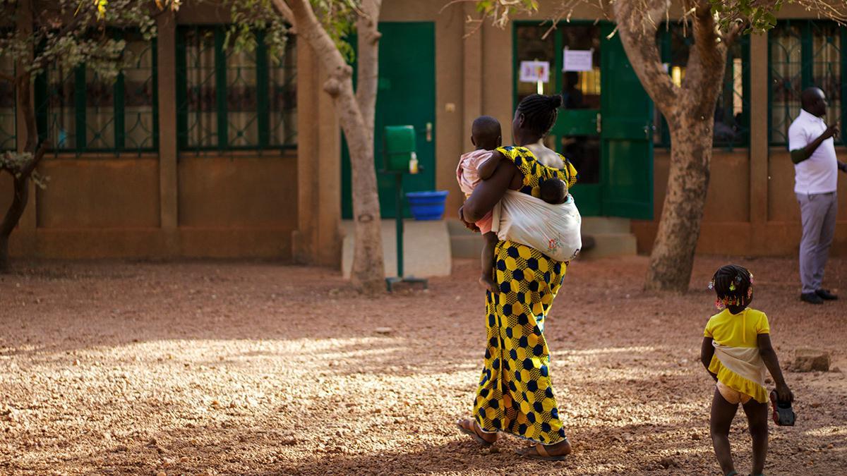 Ländliche Szene: eine traditionell gekleidete Frau aus Burkina Faso, mit 3 Kindern, zwei davon werden getragen