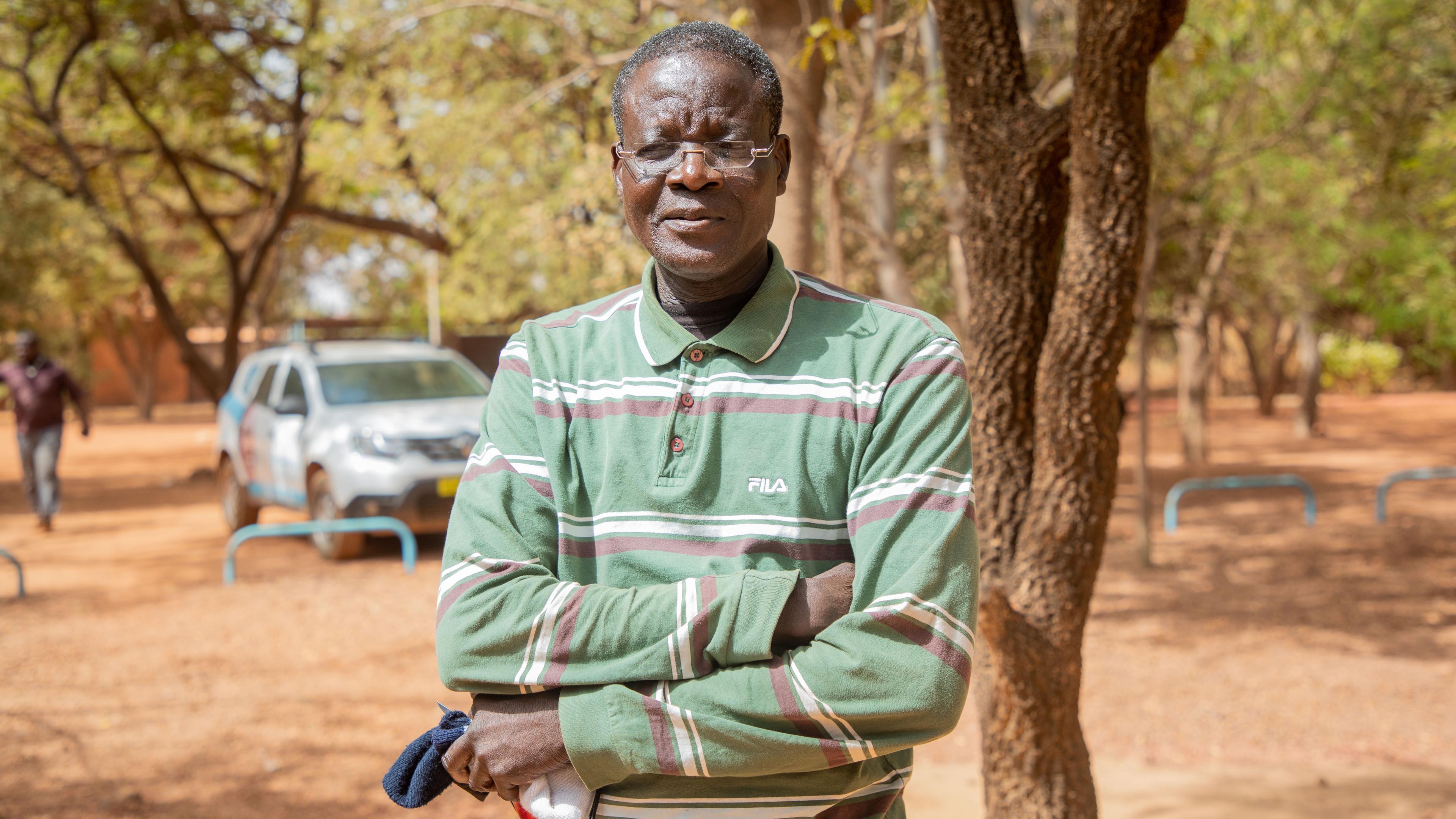 Patient from Burkina Faso with one-dollar glasses, standing in front of a tree