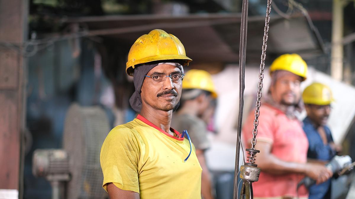 Stahlarbeiter in Indien, in einer Fabrik, trägt gelben Schutzhelm