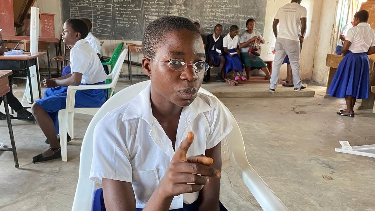 Schülerin in Malawi in Klassenzimmer beim Sehtest. Sie hält den Zeigefinger hoch, trägt EinDollarBrille