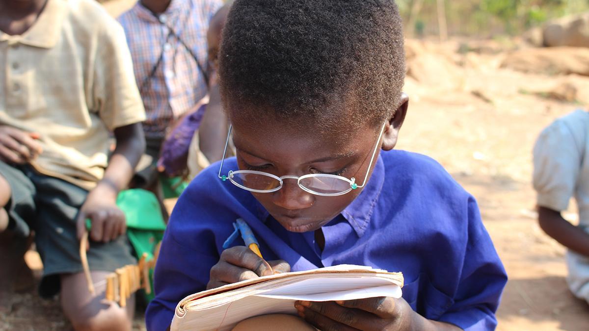 Young pupil wears OneDollarGlasses and writes in a notebook