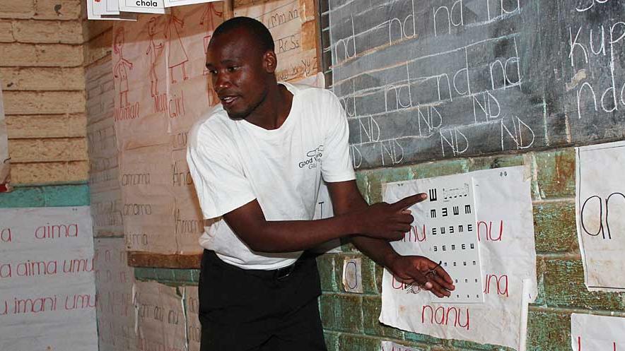 Mitarbeiter GoodVision Malawi steht an der Sehprobentafel vor einer Schulklasse