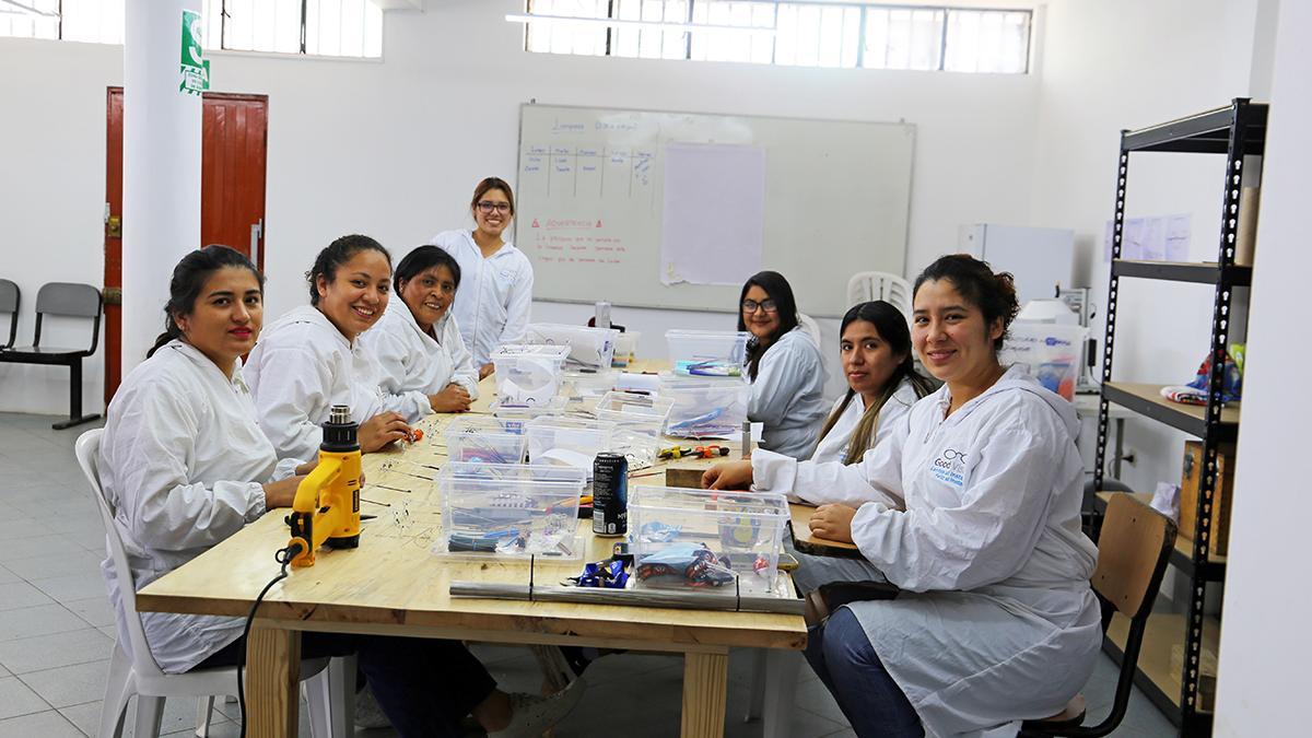 Mitarbeiterinnen von Lentes al Instante Peru, in weißen Kitteln, sitzen um einen Tisch herum