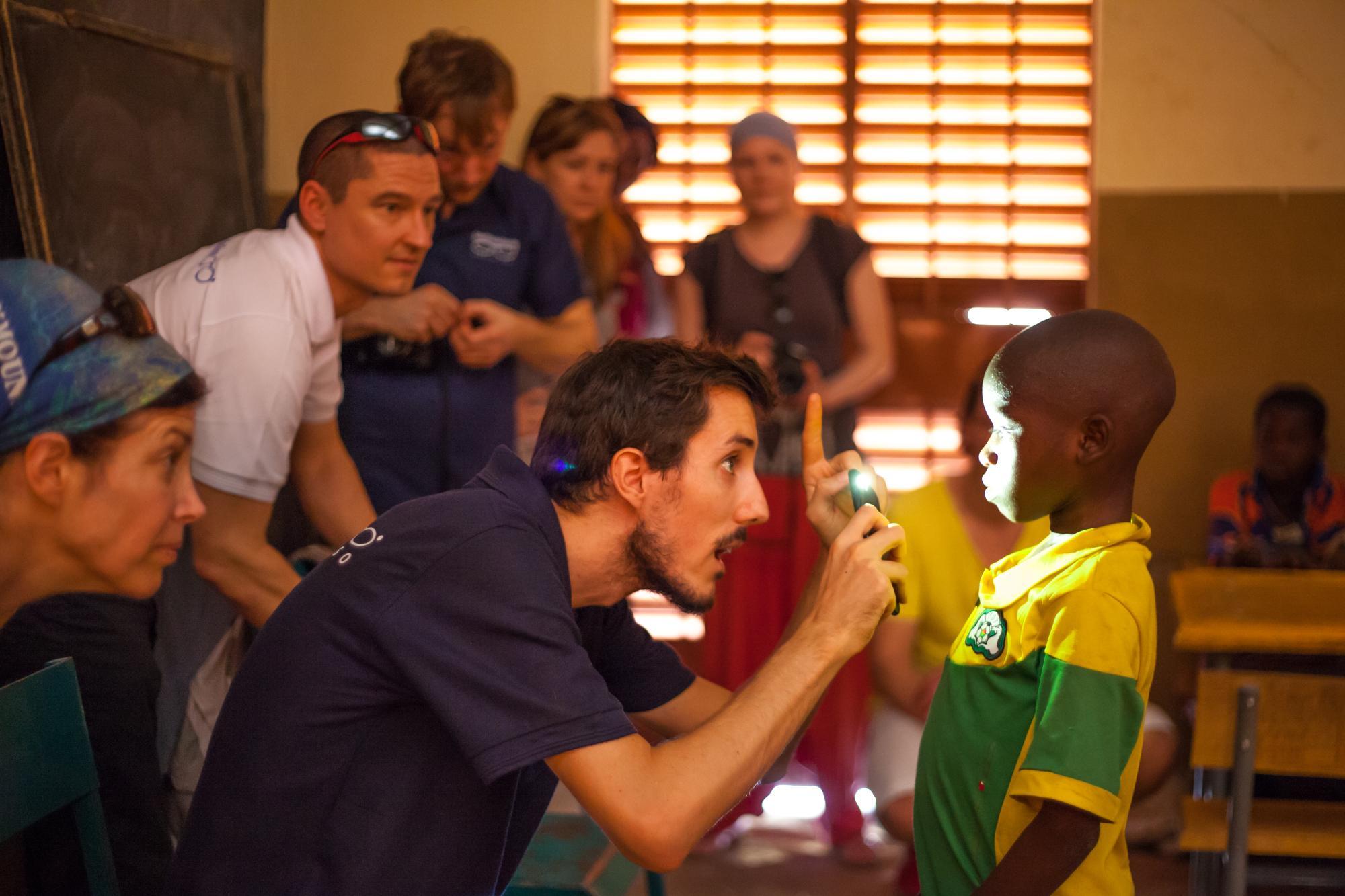 Mitarbeiter GoodVision Burkina Faso leuchtet Kind mit Taschenlampe ins Auge