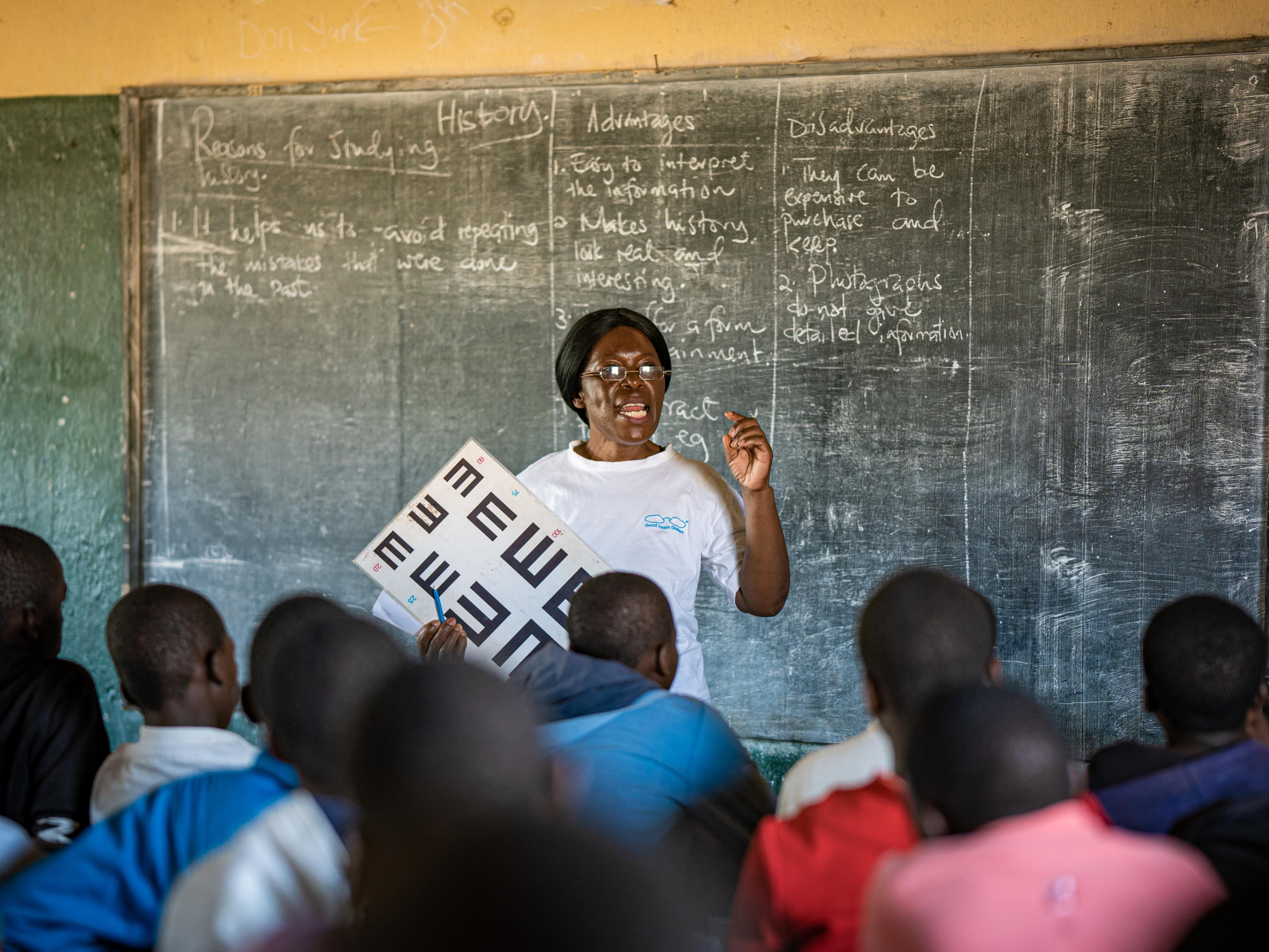 Woman with vision test chart in front of school class