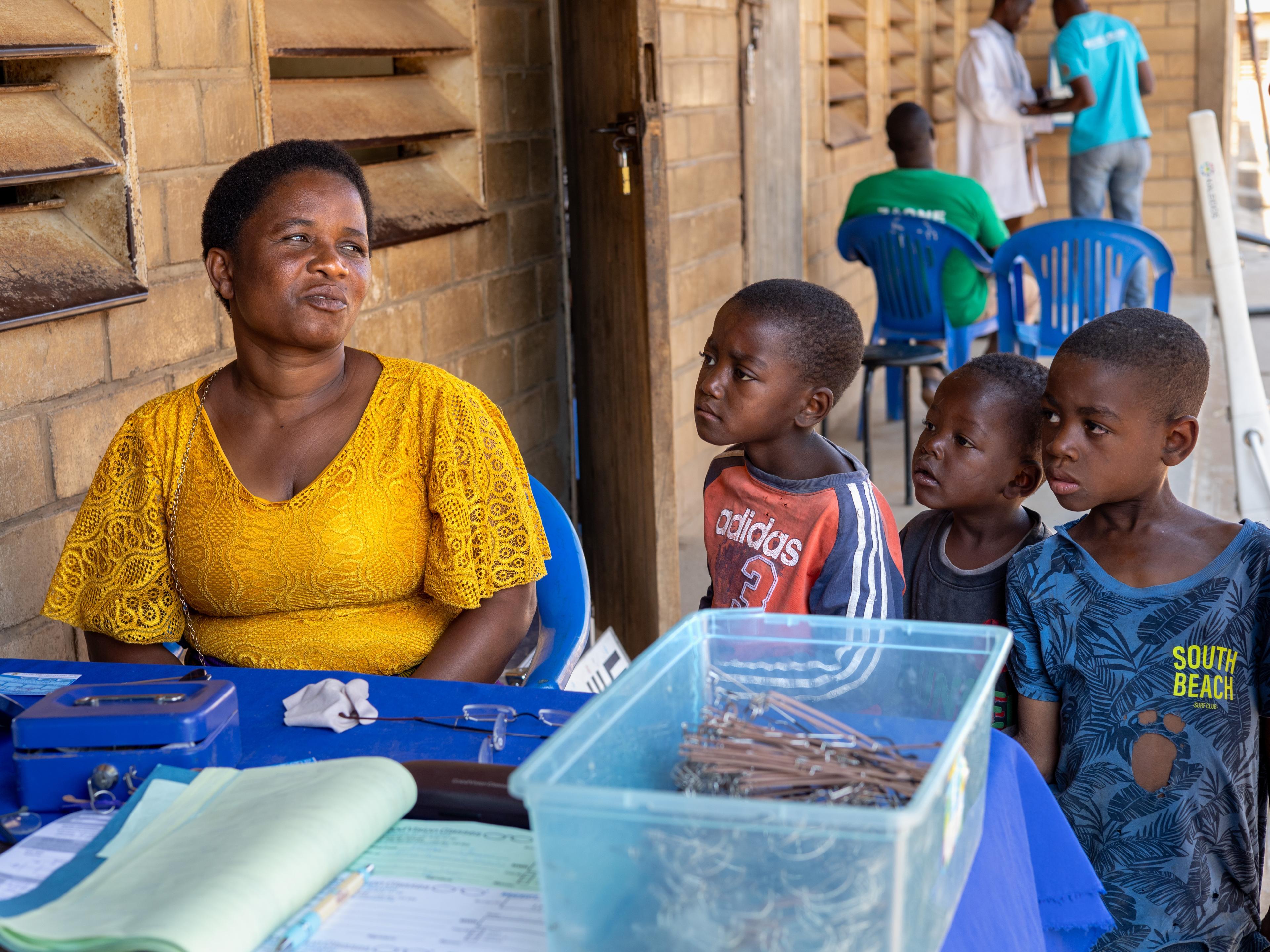 Frau am Brillenverkaufsstand von GoodVision Malawi, beobachtet von neugierigen Kindern